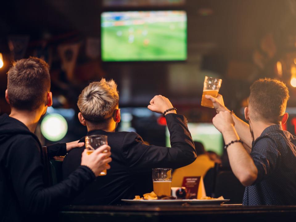 three people at a bar drinking beers and watching a sporting event