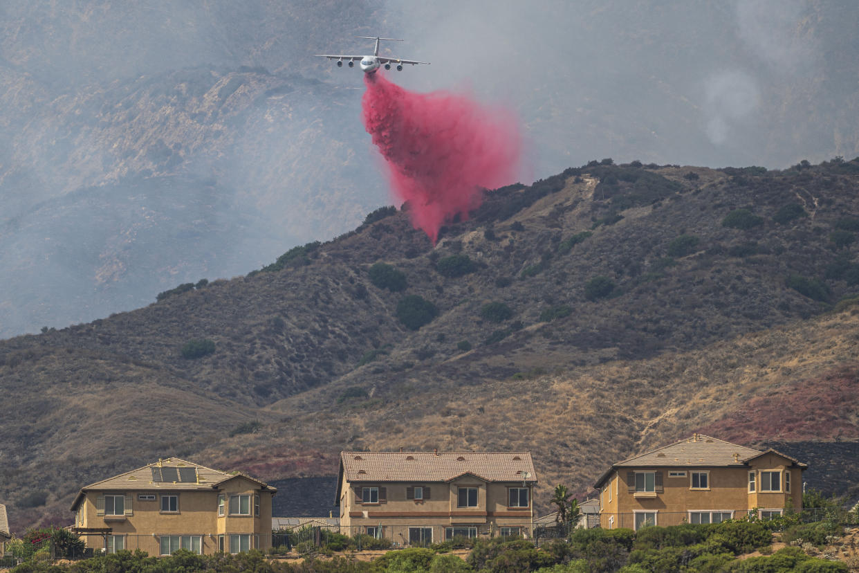 A fire tanker makes a retardant drop over a hillside.