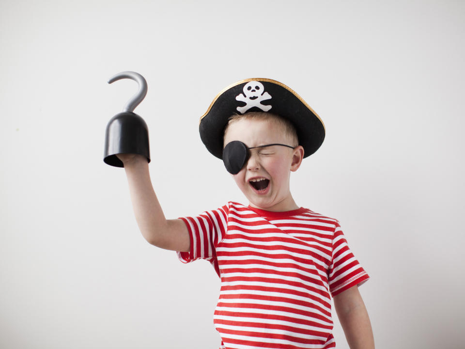 A child is enthusiastically dressed as a pirate, wearing a striped shirt, pirate hat with a skull and crossbones, an eye patch, and holding a hooked hand