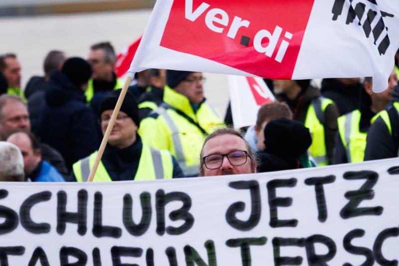 Employees of the Lufthansa Technik division demonstrate with a banner reading "!!! No more !!! With tariff difference East West" and flags in front of the departure hall in Terminal 1 of BER Airport. In the ground staff wage dispute at Germany's flagship carrier Lufthansa, technical staff began a three-day strike on Wednesday morning. Carsten Koall/dpa