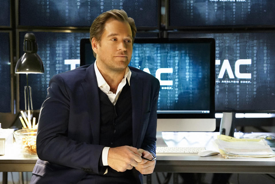 Weatherly leans against a desk while looking off-camera