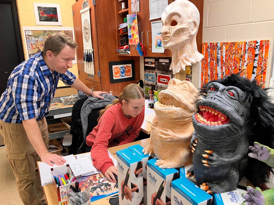 Art teacher Matt Feck helps Aubrie Kimmel upload and size her drawing in the computer program that will make it ready for printing. As the plan was to gradually print out all the motives made by the students in the class, Feck advised Kimmel to position her tree closer to his example.