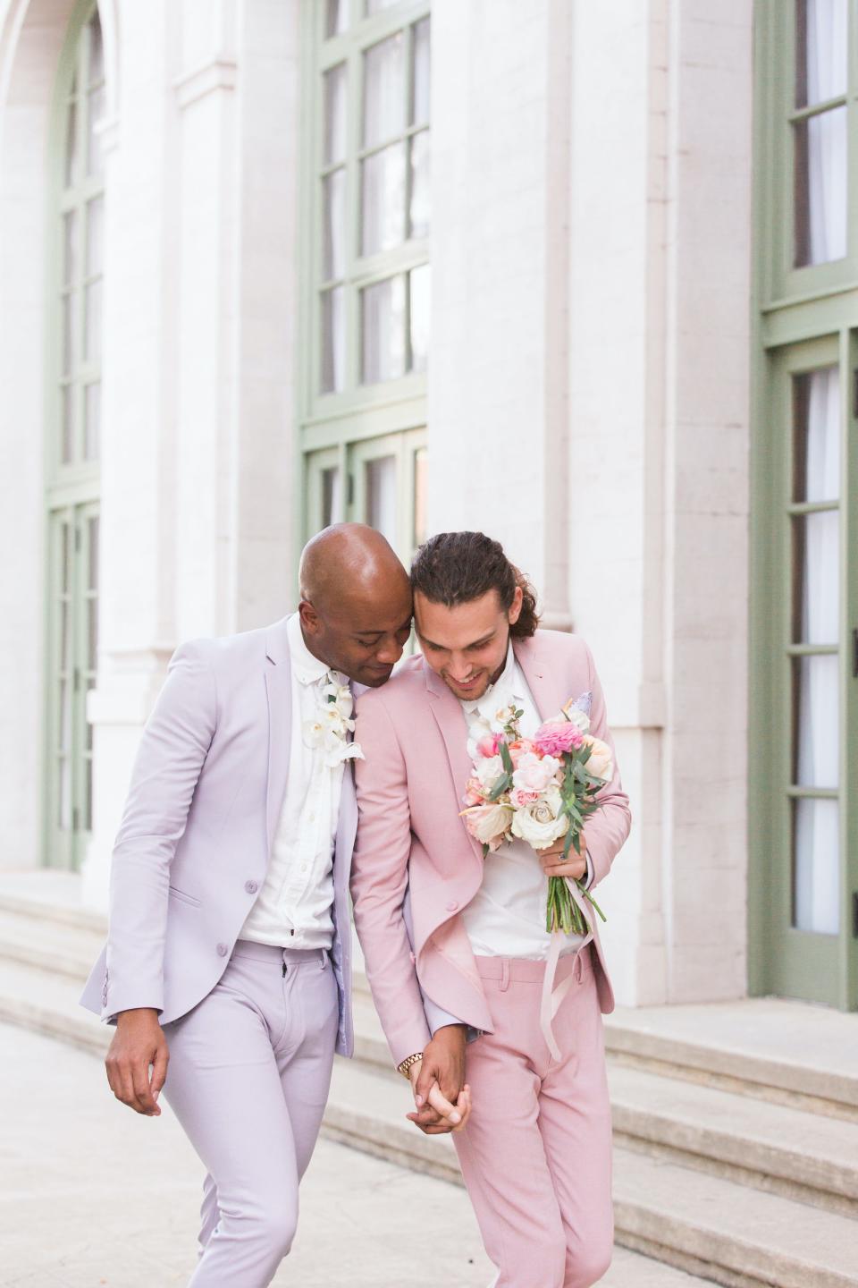 A groom puts his arm around his husband while they are both wearing pastel suits.