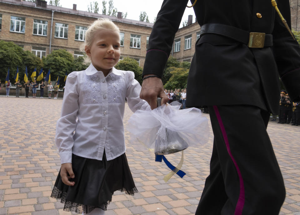 A graduate cadet holds the hand of a young schoolgirl and rings the bell on the first day of school at a cadet lyceum in Kyiv, Ukraine, Thursday, Sept. 1, 2022. (AP Photo/Efrem Lukatsky)