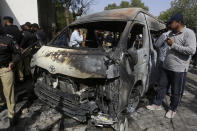Pakistani police officers and investigators examine a burned van at the site of explosion in Karachi, Pakistan, Tuesday, April 26, 2022. The explosion ripped through the van inside a university campus in southern Pakistan on Tuesday, killing several people including Chinese nationals and their Pakistani driver, officials said. (AP Photo/Fareed Khan)