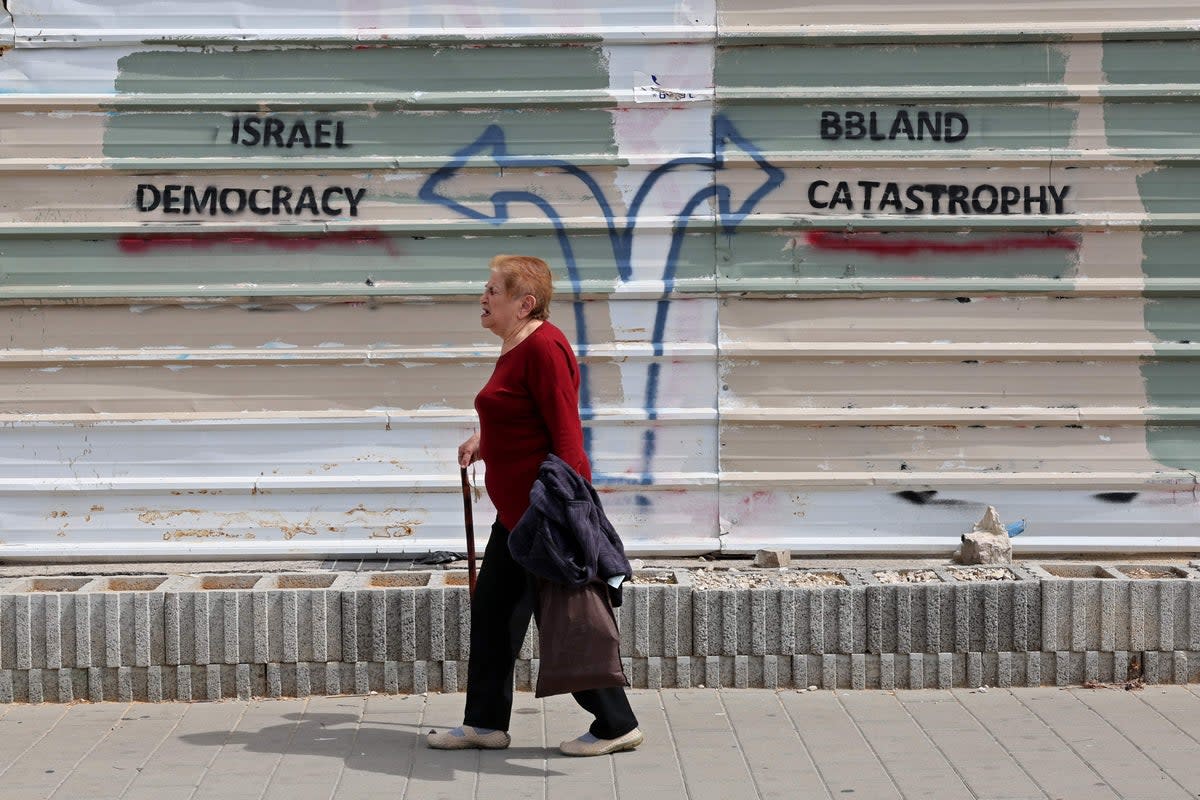 A woman walks past a graffiti during ongoing demonstrations in Tel Aviv on Thursday (AFP via Getty Images)