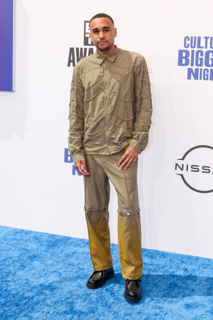 Speedy Morman stands on the blue carpet at Culture's Biggest Night event, wearing a unique tan outfit with intricate detailing