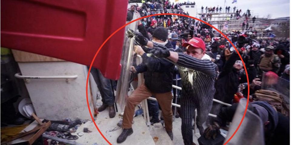 A man wearing a pinstripe costume and Make America Great Again red hat throwing a large red plastic pylon amid a crowd