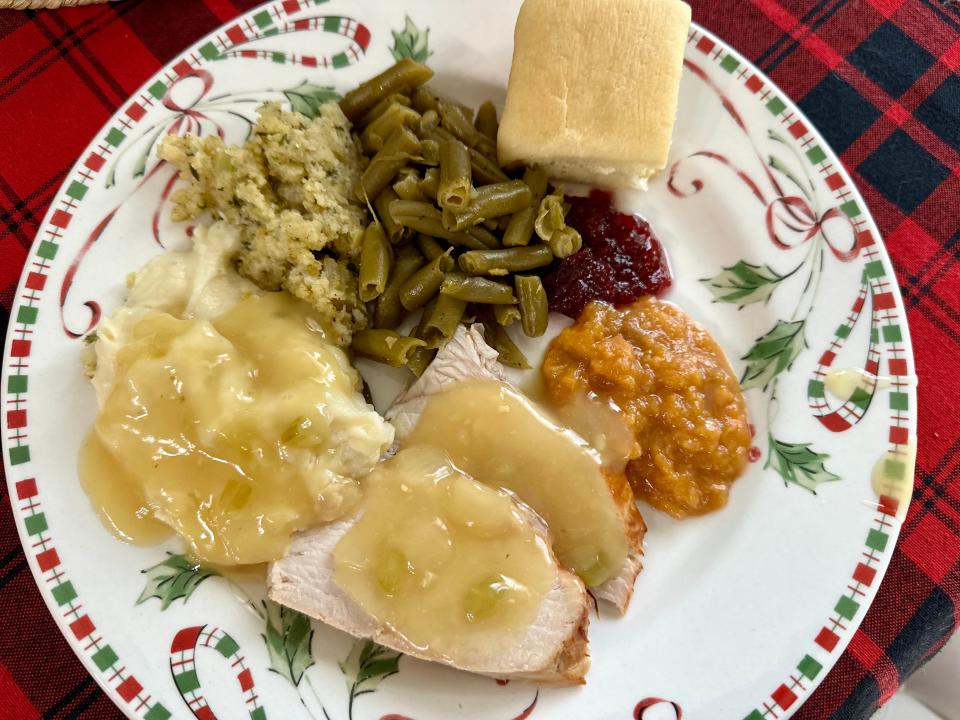 Plate with a roll, turkey, mashed potatoes, green beans, stuffing, and cranberry sauce