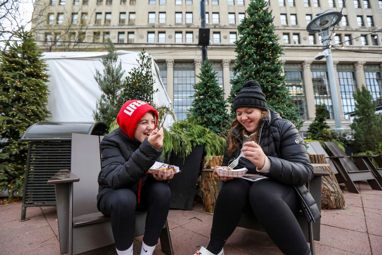 Alexa Stubbe, 12, of Livonia, left, and Jaelyn Stubbe, 12, of Lincoln Park enjoy chocolate-covered waffles from the Waffle Cabin during the Downtown Detroit Markets at Cadillac Square in downtown Detroit on Wednesday, Nov. 22, 2023.
