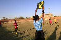 In this Wednesday, Dec. 11, 2019 photo, a referee holds a board as Sudanese al-Difaa, in pink, and al-Sumood women teams play in Omdurman, Khartoum's twin city, Sudan. The women's soccer league has become a field of contention as Sudan grapples with the transition from three decades of authoritarian rule that espoused a strict interpretation of Islamic Shariah law. (AP Photo)