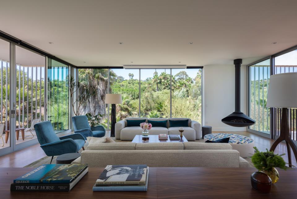 Two low, cream-colored sofas anchor the living area, surrounding a vintage gold mirror-based cocktail table with a rosewood top and two midcentury Italian chairs. A custom ottoman topped with Hermès fabric for Dedar and a tree trunk-shaped floor lamp by West Hollywood designer Robert Kuo accent a room that includes a floating fireplace and a custom silk-cashmere rug.