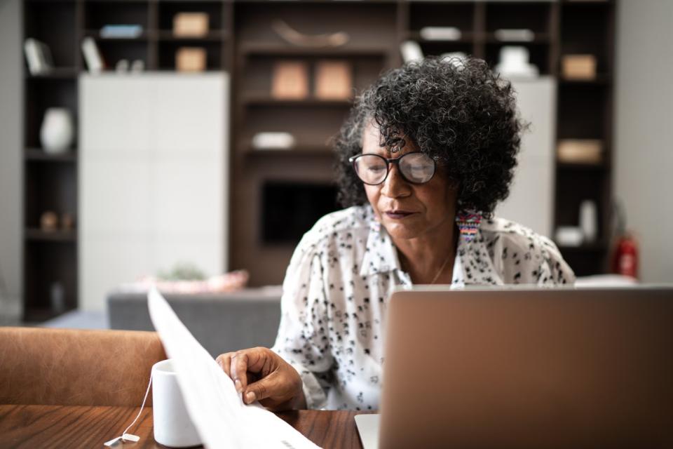 Person looking at laptop and paperwork.