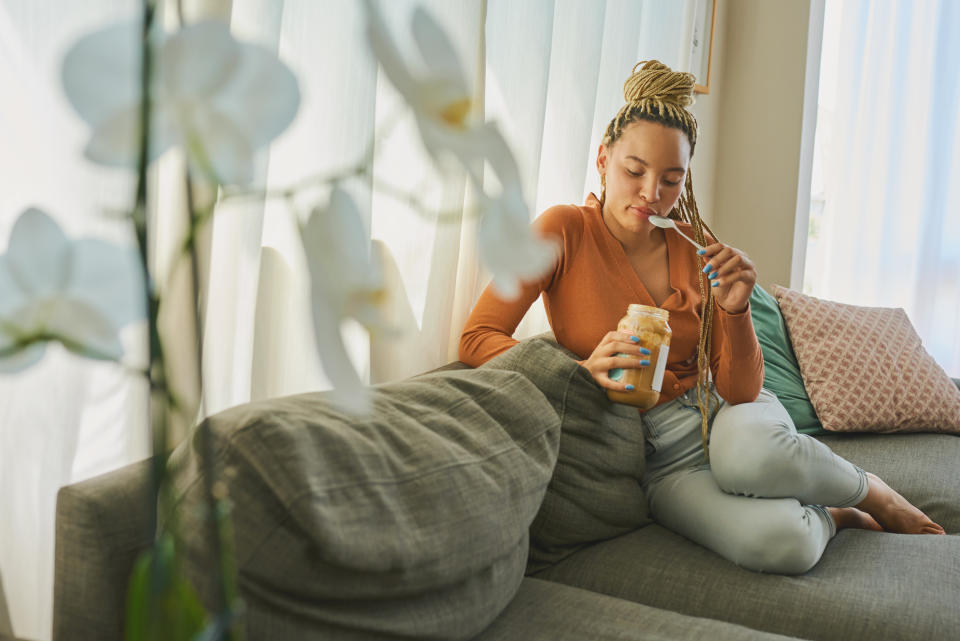 a woman sitting on the couch and eating a jar of peanut butter