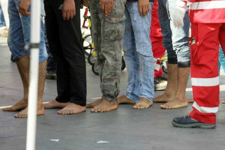 Barefoot migrants queue to disembark from a military vessel in the port of Palermo on August 6, 2015