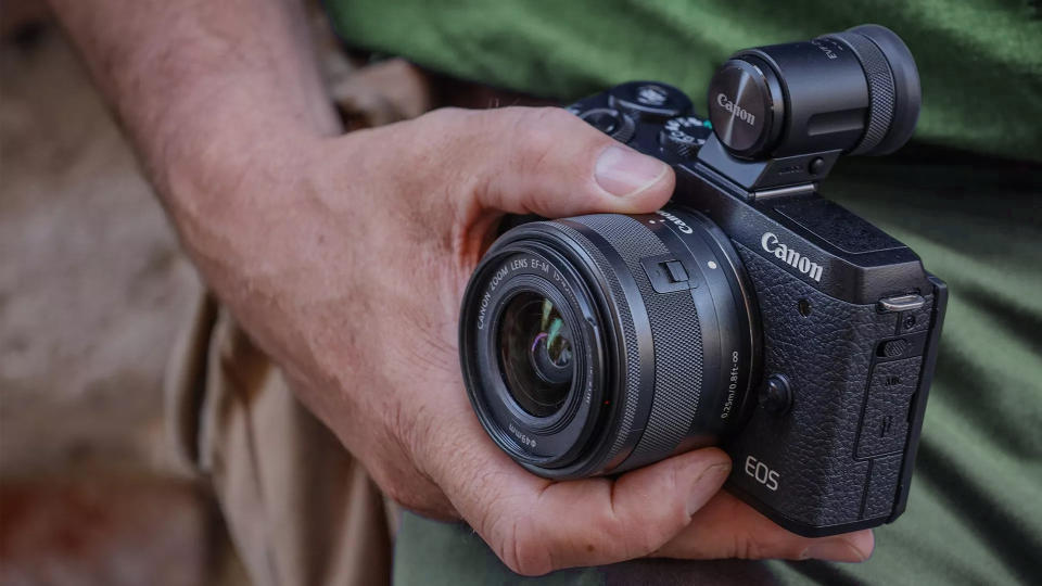 Close up of a Canon EOS M6 Mark II being held by a photographer wearing a green top