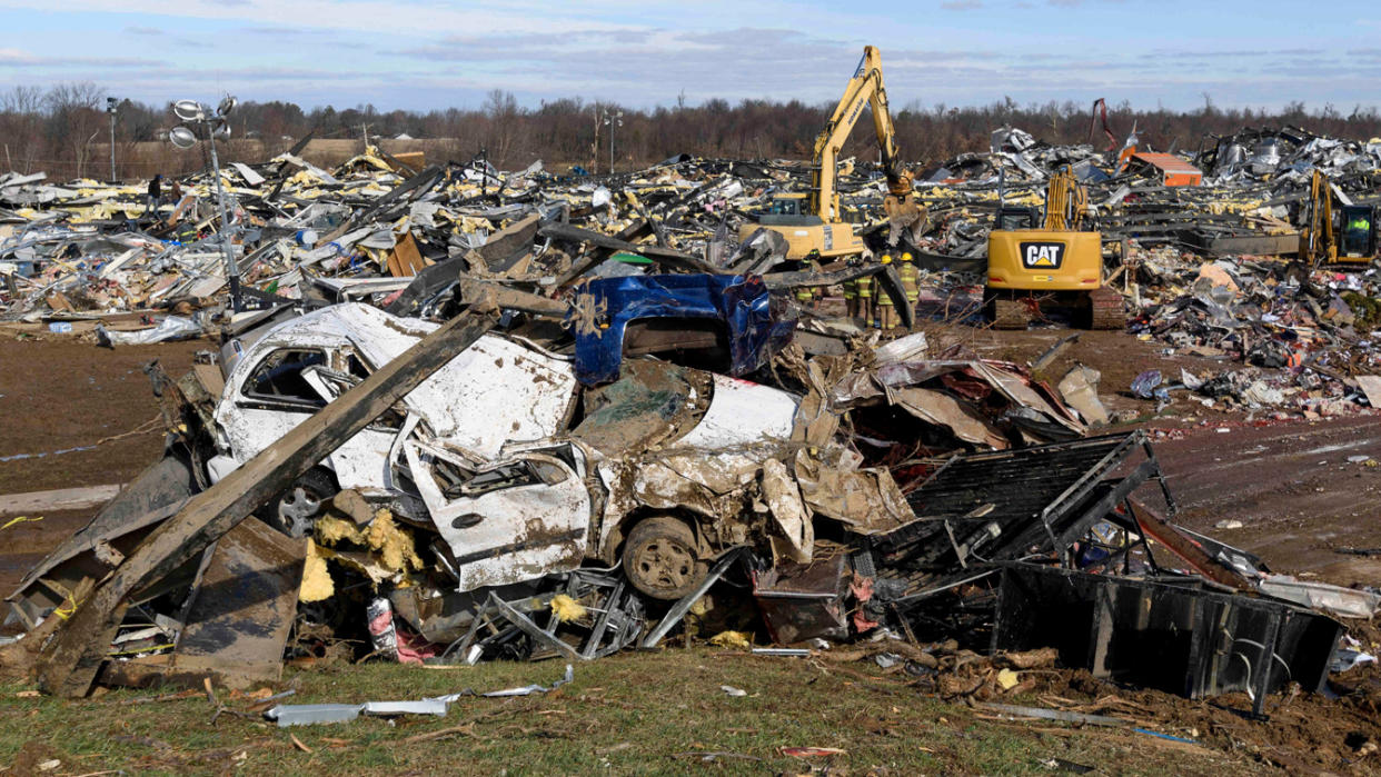 A flattened car and a large field of debris at the destroyed Mayfield Consumer Products candle factory.
