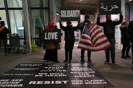 Protesters hold signs in opposition to U.S. President Donald Trump's ban on immigration and travel outside Terminal 4 at JFK airport in Queens, New York City, New York, U.S. January 29, 2017. REUTERS/Joe Penney