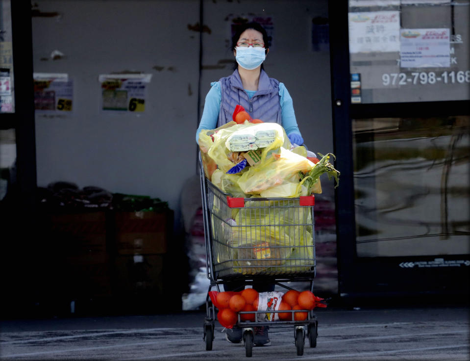 Wearing a mask amid concerns of the spread of COVID-19 a woman pushes a basket full of groceries out of a store in Richardson, Texas, Wednesday, April 1, 2020. (AP Photo/LM Otero)