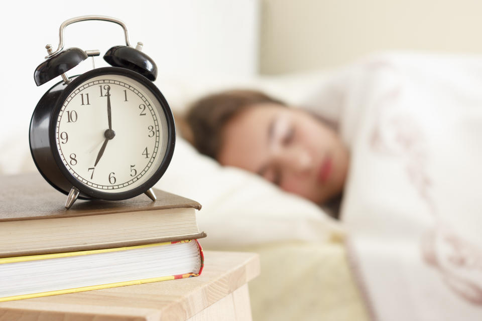 Teenager girl sleeping in a white bed. Alarm clock in the foreground on pile of books