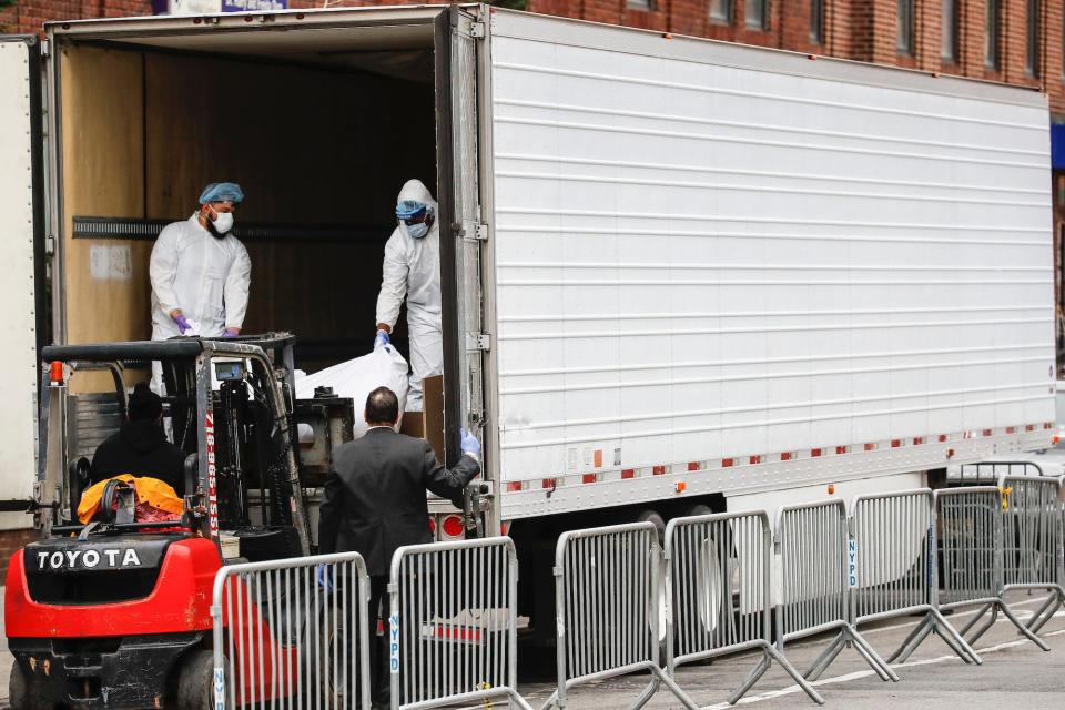 A body wrapped in plastic is loaded onto a refrigerated container truck used as a temporary morgue by medical workers wearing personal protective equipment due to COVID-19 concerns.