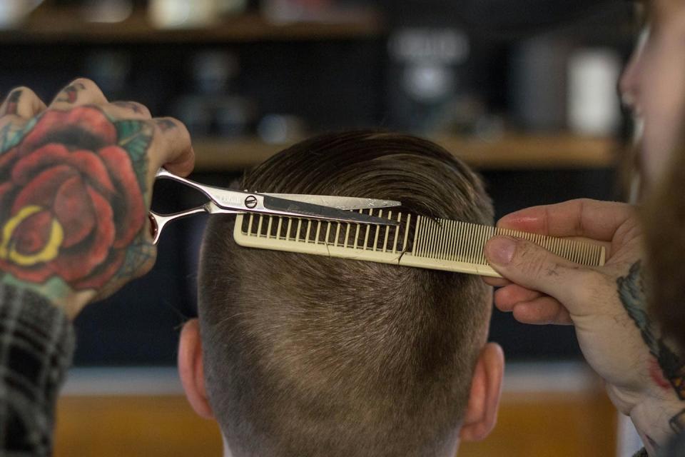 A hairdresser with comb and scissors cuts hair very short.