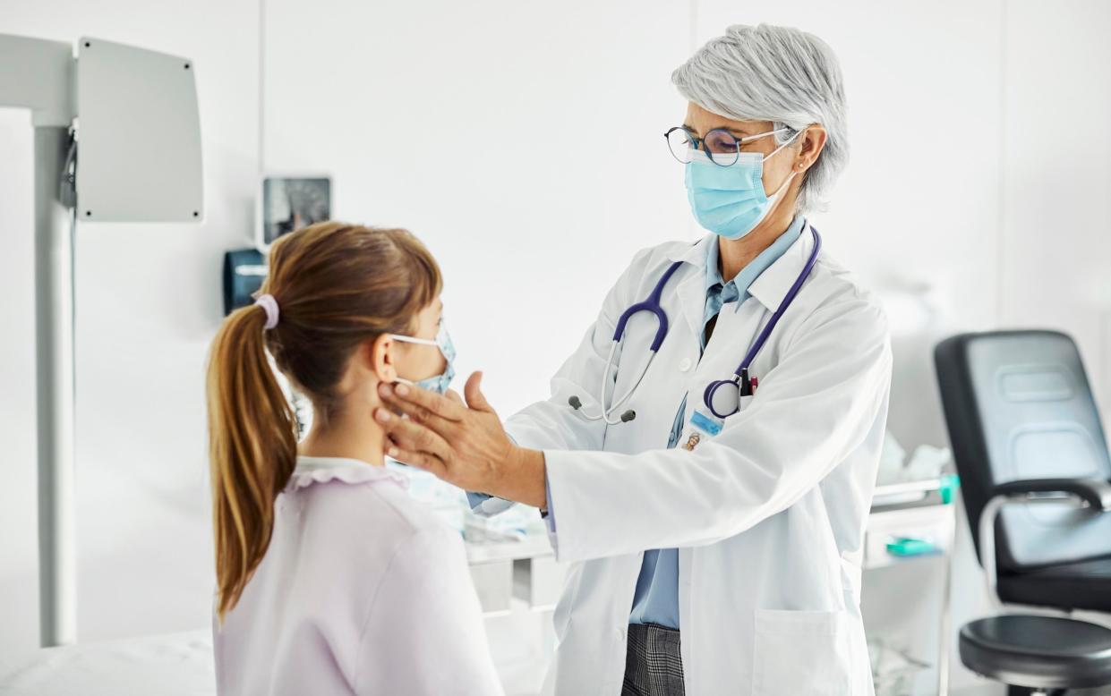 A doctor wearing a mask examines a young girl