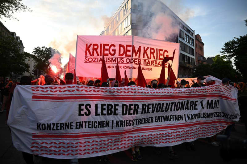People hold up a banner with the words "War against war" and set off pyrotechnics in the process "Revolutionary May Day demonstration".  Sebastian Gollnow/dpa