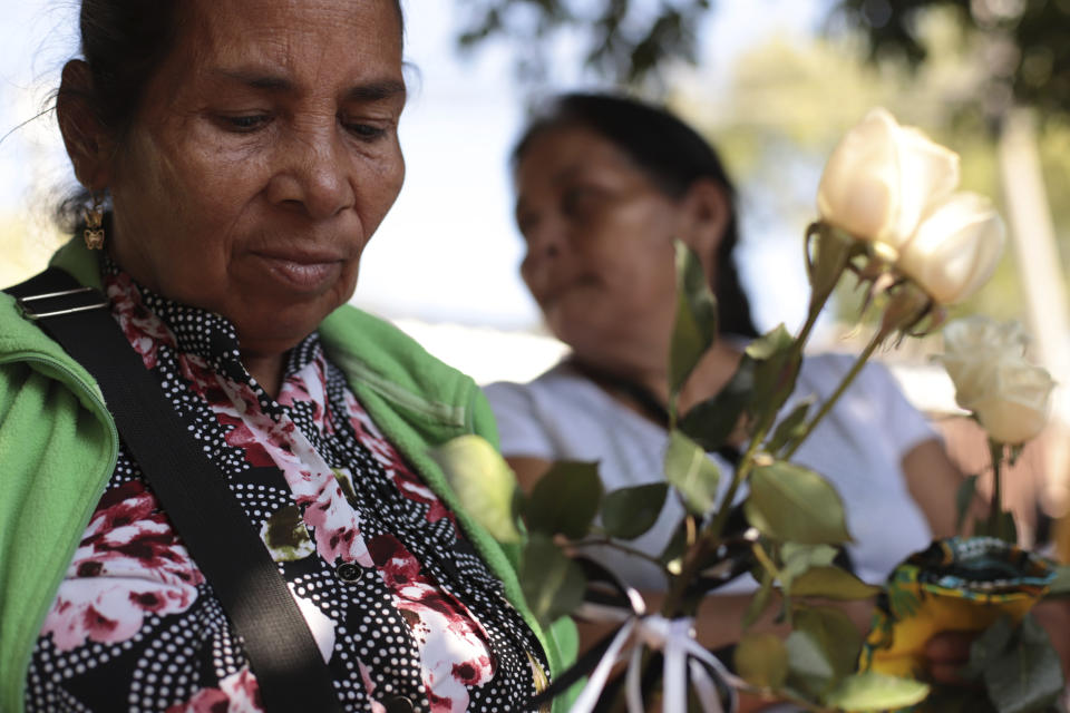 Juana de Jesús Bonilla Realegeño, de 66 años, sostiene rosas blancas mientras espera con sus familiares para recibir seis pequeños ataúdes que contienen restos de los familiares que perdió en una masacre de 1982, en San Salvador, El Salvador, el jueves 23 de enero de 2020. (AP Foto/Salvador Melendez)