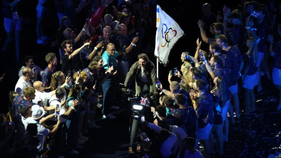 Cruise stands on the motorbike as he rides through a corridor of spectators