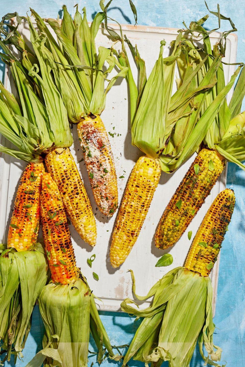 three types of grilled corn on a white wooden serving board