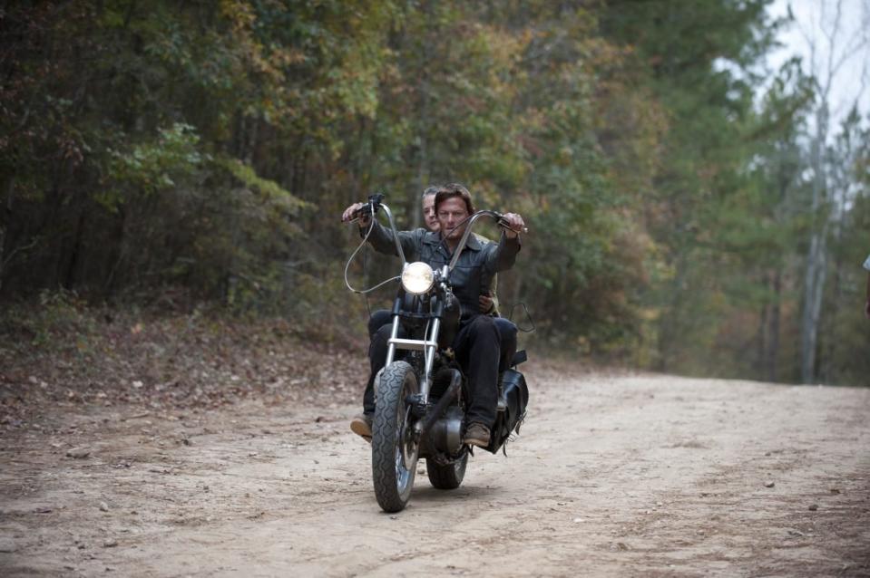 Daryl rides down a dirt road on his motorcycle with Carol on the back 