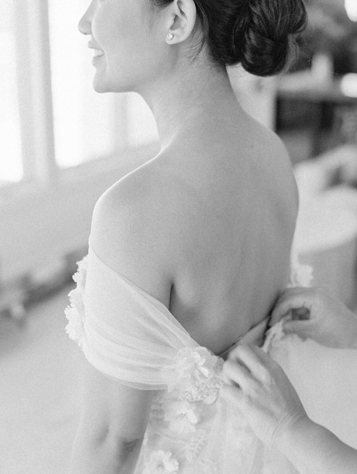 bride putting on off the shoulder wedding dress