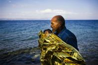 A elderly man carries a child in a blanket after arriving by boat on the Greek island of Lesbos, after crossing the Aegean sea from Turkey, on October 9, 2015