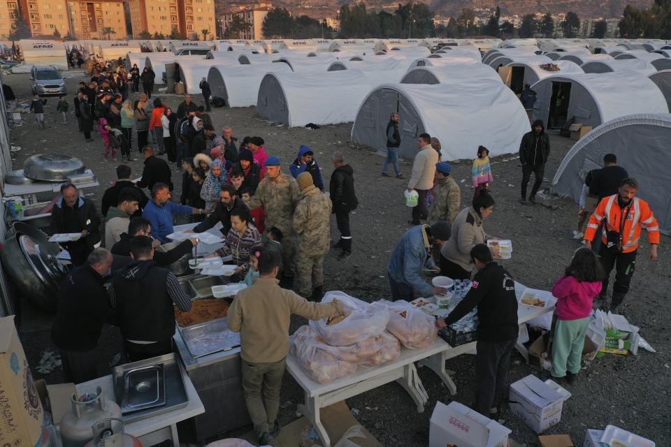 FILE - People who lost their houses in the devastating earthquake, lineup to receive food at a makeshift camp, in Iskenderun city, southern Turkey, on Feb. 14, 2023. Hundreds of thousands of people are seeking shelter after the Feb. 6 earthquake in southern Turkey left homes unlivable. Many survivors have been unable to find tents or containers dispatched to the region by the government and aid agencies, Instead they have sought refuge in any structure that can protect them from the winter conditions, including greenhouses, rail carriages and factories. (AP Photo/Hussein Malla)