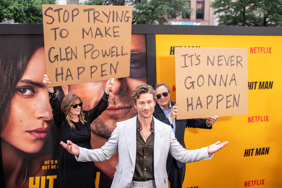 Glen Powell parents hold up signs behind him as they attend the special screening of 