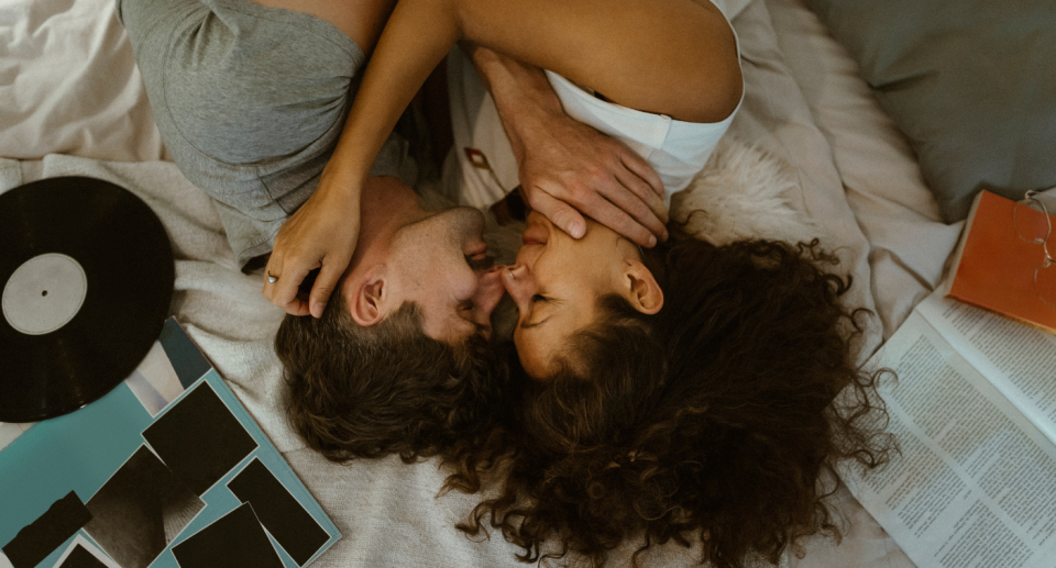 A couple lying down and kissing on a bed with a record nearby.