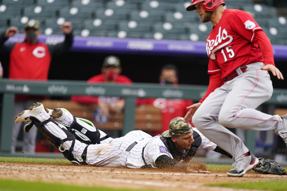 Colorado Rockies catcher Dom Nunez, left, reaches out to recover the ball after a wild pitch from reliever Jordan Sheffield (not shown) allowed Cincinnati Reds' Nick Senzel, right, to score from third base in the ninth inning of a baseball game Sunday, May 16, 2021, in Denver. (AP Photo/David Zalubowski)