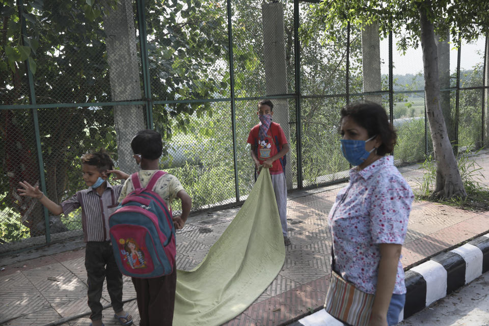 Children lay a sheet to sit on for their class on a sidewalk as their teacher Veena Gupta watches in New Delhi, India, on Sept. 3, 2020. Veena Gupta and her husband Virendra Gupta are conducting free classes for underprivileged children on a sidewalk in New Delhi with the goal to keep them learning and not left behind when schools reopen. It all began when Veena's maid complained that with schools shut, children in her impoverished community were running amok and wasting time. As most schools in India remain shut since late March when the country imposed a nationwide lockdown to curb the spread of COVID-19, many switched to digital learning and taking classes online. (AP Photo/Manish Swarup)