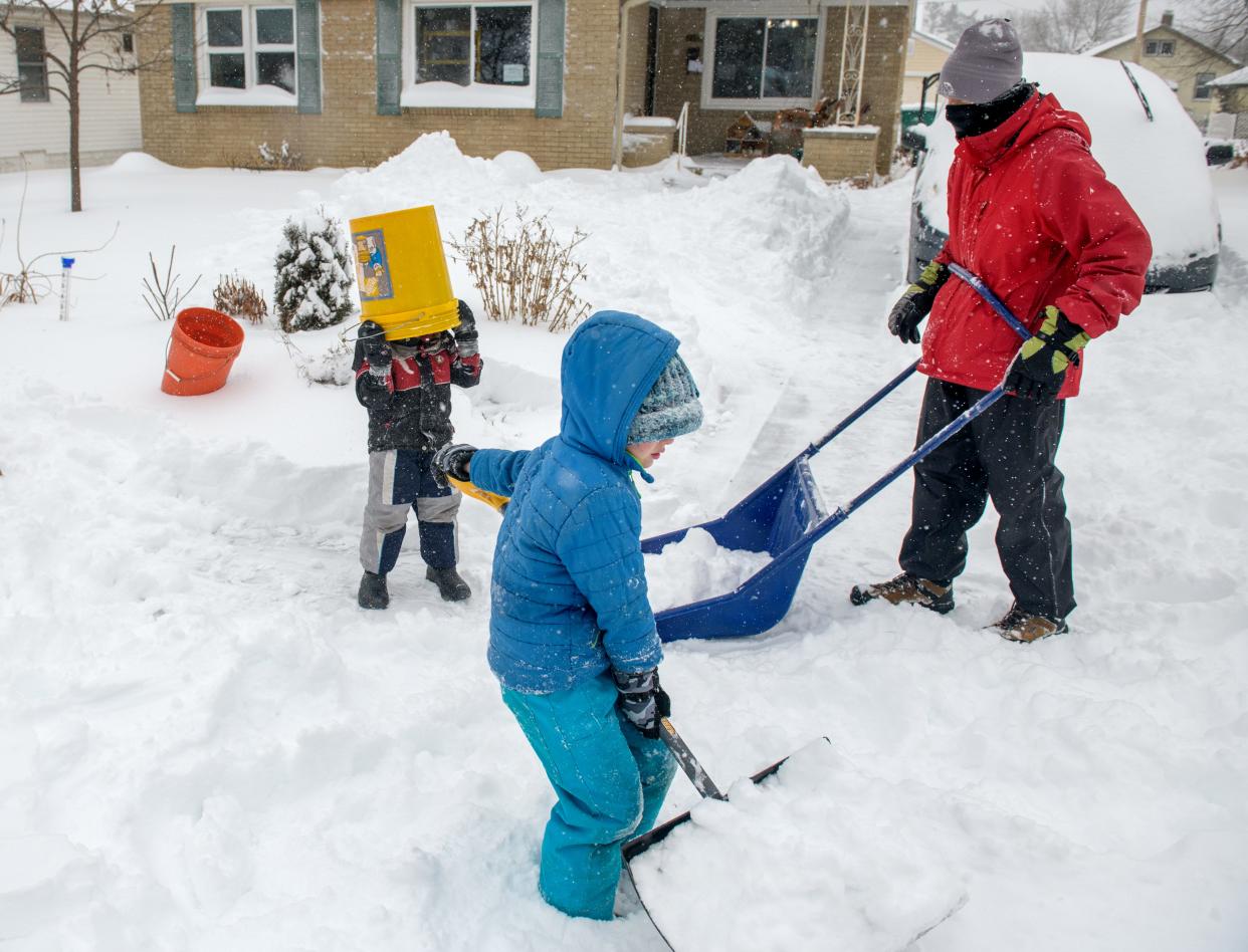 John Havenga, in red coat, and two of his four kids, Ezra, 4, with a bucket on his head, and Gideon, 7, work at shoveling snow and having some fun at their house on Laura Street in West Peoria on Wednesday, Feb. 2, 2022. Havenga's other kids, Micah, 9, and Daniel, 11, also helped out.