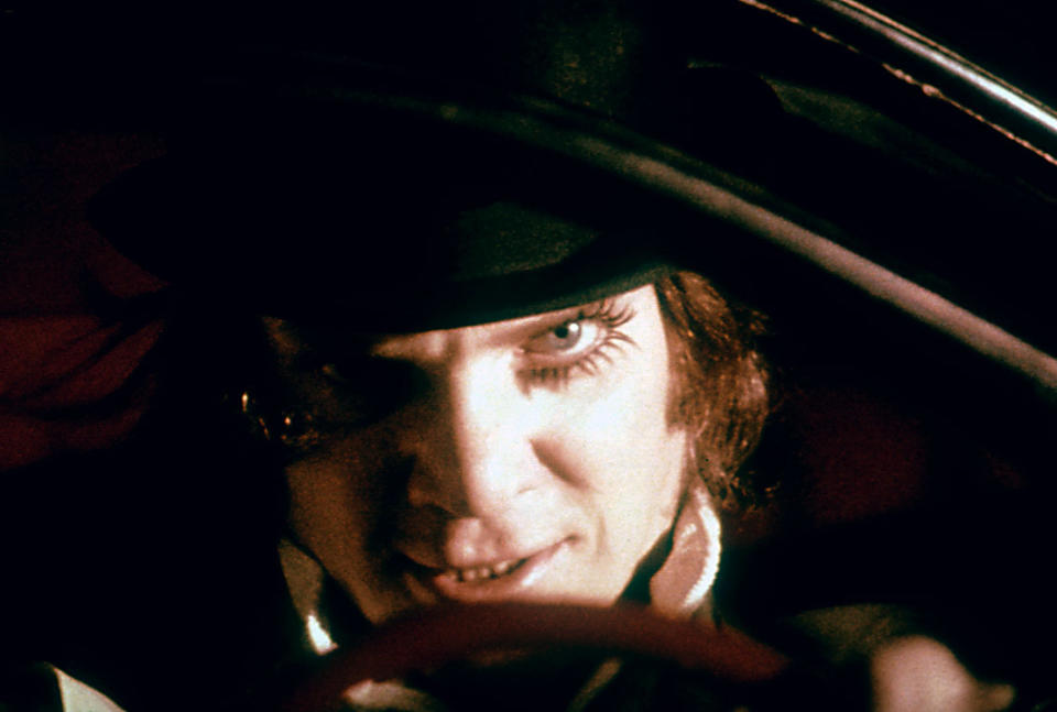 Alex from "A Clockwork Orange" smiling and peeking out from under the brim of his hat
