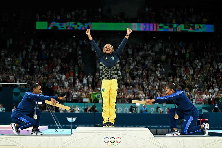 La estadounidense Simone Biles (plata) y su compatriota Jordan Chiles (bronce) parecen rendirse a los pies de la brasileña Rebeca Andrade (oro) durante la ceremonia del podio de ejercicios de suelo femenino de gimnasia artística