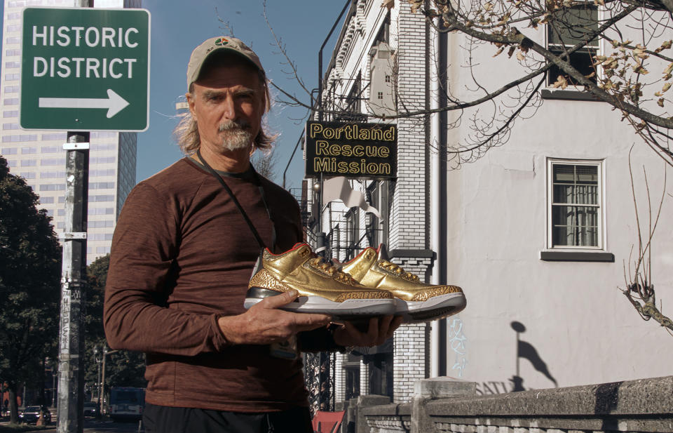 This photo provided by the Portland Rescue Mission shows James Free posing for a photo with a pair of of gold Nike Air Jordan 3 sneakers at the Portland Rescue Mission on Sunday, Oct. 30, 2023, in Portland, Ore. A pair of rare Nike sneakers donated to a homeless shelter in Portland, Oregon, are up for auction and are expected to raise as much as $20,000. Why? They were custom-made for filmmaker Spike Lee. (Aaron Ankrom/Portland Rescue Mission via AP)