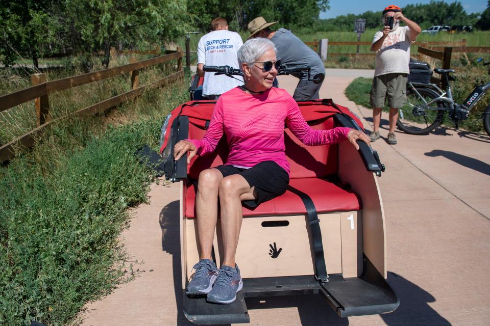 Ann Lahde, a pilot with Cycling Without Age, shows how passengers should sit on a trishaw bike at the Signature Bluffs Trail head in Greeley on Thursday, Aug. 4, 2022. 