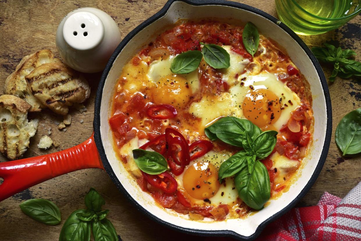 Shakshouka - traditional dish of israeli cuisine from tomatoes and eggs in a skillet on a rustic wooden background. Top view with copy space.