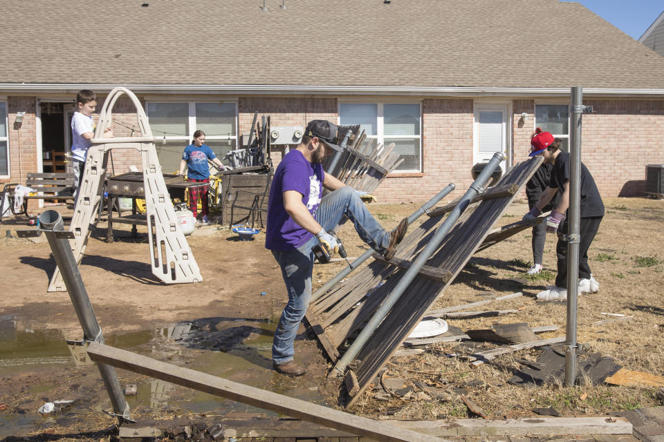 Jacob Young, front, and his family works to remove debris from their back yard on Monday, Feb. 27, 2023 in Norman, Okla. after a tornado passed through the area. The damage came after rare severe storms and tornadoes moved through Oklahoma overnight. (AP Photo/Alonzo Adams)