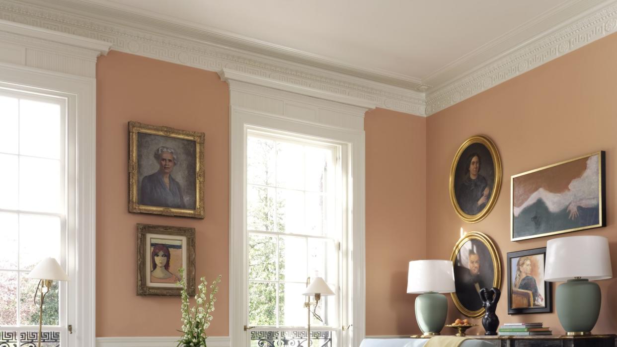 living room, orange walls, art on walls, maroon ottoman, green cushions