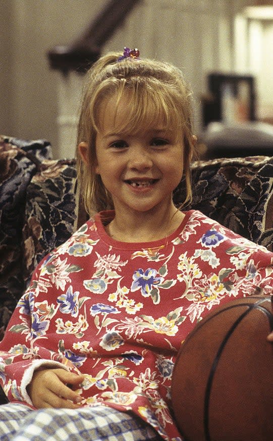 Young Morgan sitting on a couch with a basketball, wearing a floral sweater and checkered pants, smiling at the camera