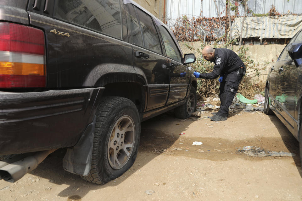 An Israeli police officer collects evidence from a vandalized vehicle in the Sheikh Jarrah neighborhood of east Jerusalem, Friday, Nov. 19, 2021. Residents from the tense Jerusalem neighborhood say the car tires of 11 Palestinian-owned vehicles were slashed by Israeli settlers. Palestinian families from the neighborhood are currently embroiled in a high-profile eviction case against Israeli settlers. (AP Photo/Mahmoud Illean)