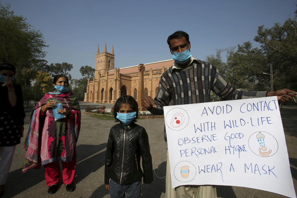 A Christian family holds a placard regarding the precautions for the newcoronavirus while they arrive to attend Sunday Mass at St. John's Cathedral in Peshawar, Pakistan Sunday, March 15, 2020. For most people, the new coronavirus causes only mild or moderate symptoms. For some, it can cause more severe illness, especially in older adults and people with existing health problems. (AP Photo/Mohammad Sajjad)